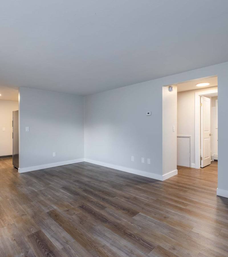 Spacious living area with wood-style flooring and bright walls, open layout inviting natural light at Presidential Estates in Rochester, New York