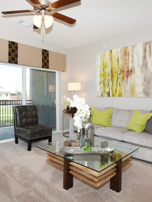 Model living room with a ceiling fan and private balcony access at Outlook Ridge in Pueblo, Colorado
