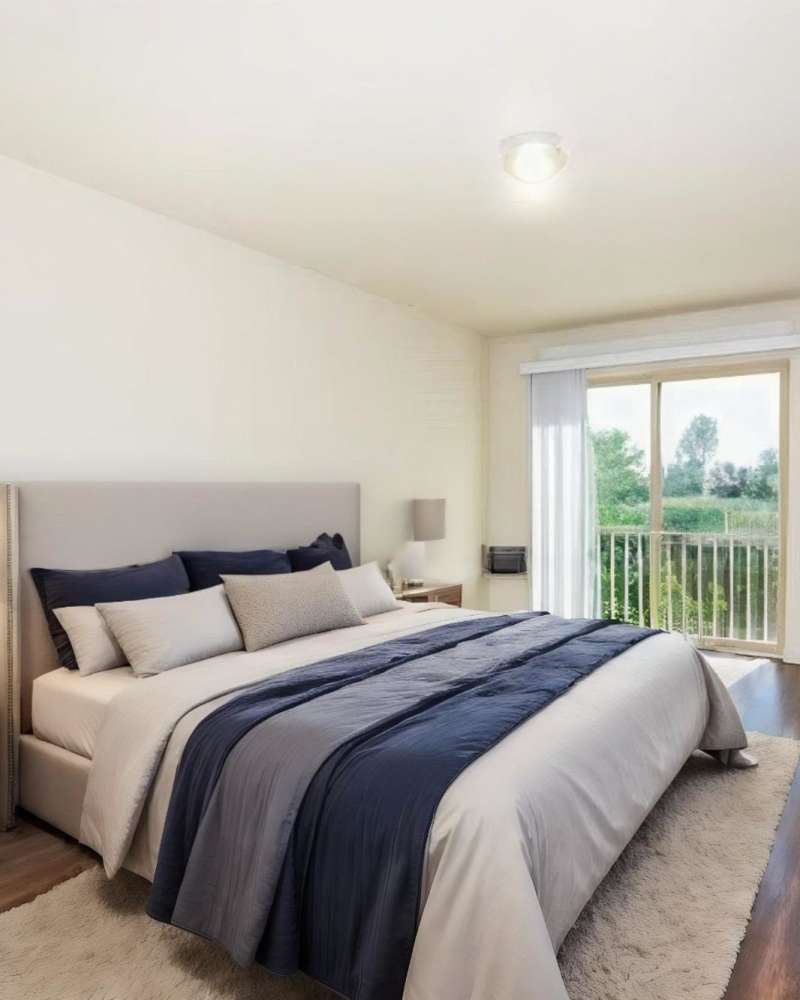 Bedroom with a bed and a sliding door leading to the private balcony at Blanton Commons in Beaverton, Oregon
