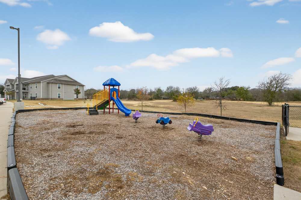 Charming playground with colorful equipment surrounded by open green spaces at Lakewood Crossing in Granbury, Texas.