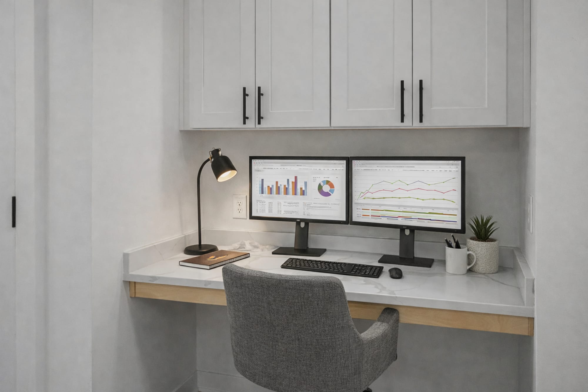 Built-in work-from-home desk in The Cobb 1-bedroom floor plan at The Carillon in Nashville, TN with quartz-style countertop, overhead cabinets, task lighting, and dual-monitor workspace.