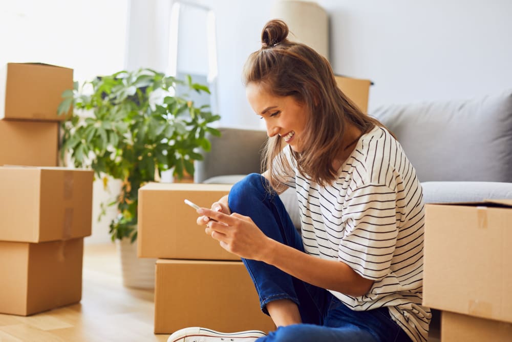 A woman takes a look at her phone while unpacking during a move near Our Self Storage. 