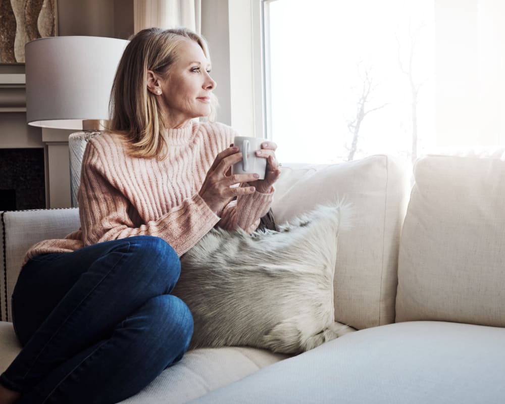 Resident enjoying coffee while sitting on her couch at Eagle Rock Apartments at Woodbury in Woodbury, New York