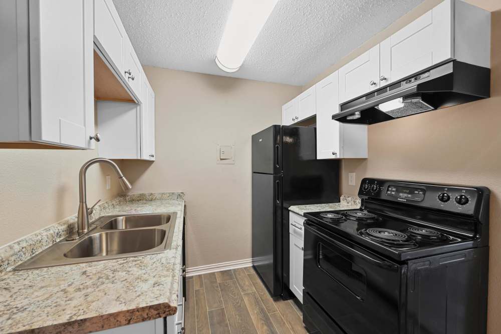 Fully equipped kitchen with granite countertops stainless steel appliances like a refrigerator, stove, and drawer microwave at Village Square in Irving 