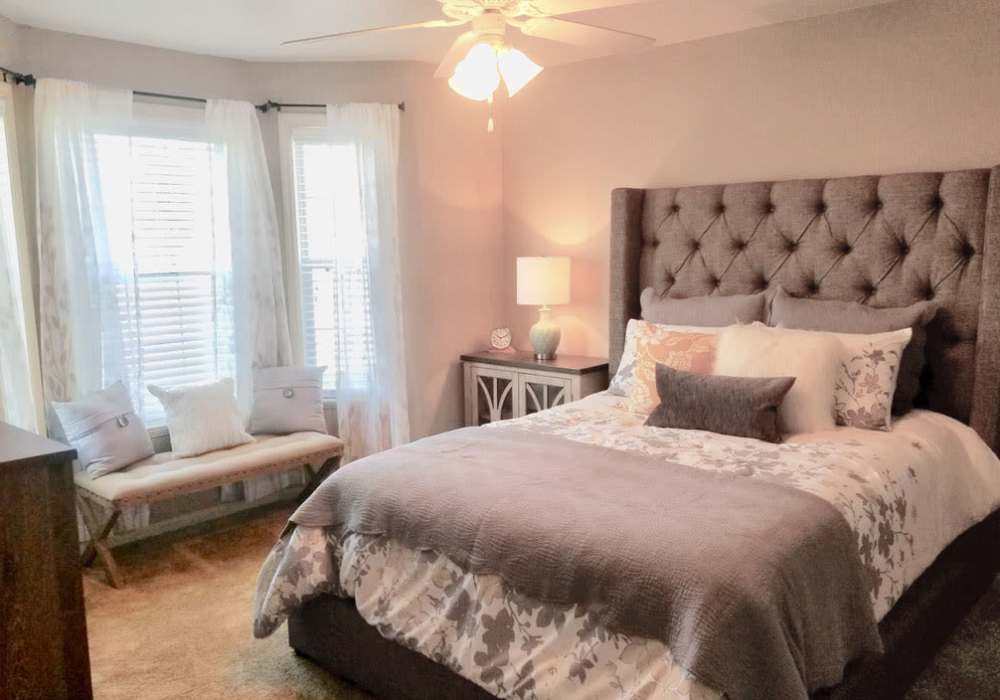 Spacious bedroom with ceiling fan, side table lamp and large window at The Reserve at Kanapaha in Gainesville, Florida