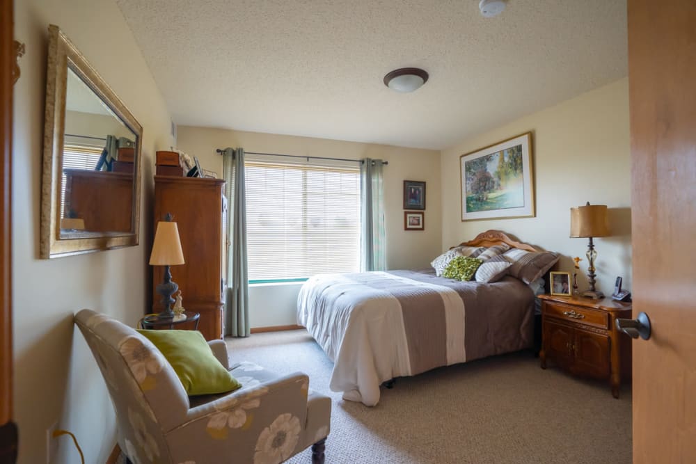 One bedroom senior  unit with a bed, large window, dresser and chair at Meadows on Fairview in Wyoming, Minnesota