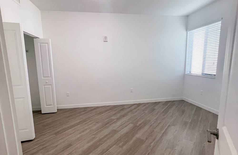 Model bedroom with large window and wood-style flooring at Park Apartments in Homestead, Florida