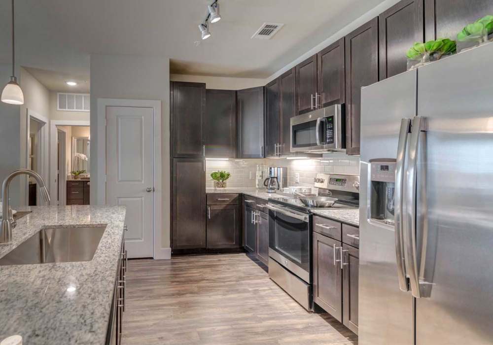 Kitchen with dark cabinets, stainless steel appliances, granite countertop and track lighting at Southfork Lake in Manvel, Texas