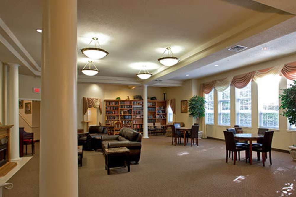 Spacious community lounge with comfortable seating, bookshelves, and natural light from large windows at Evergreen Senior Community in Bowie, Maryland