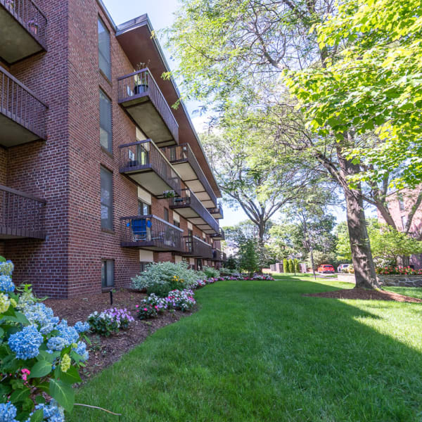 Outside view of a brick apartment building with flower beds outside at Quincy Commons in Quincy, Massachusetts