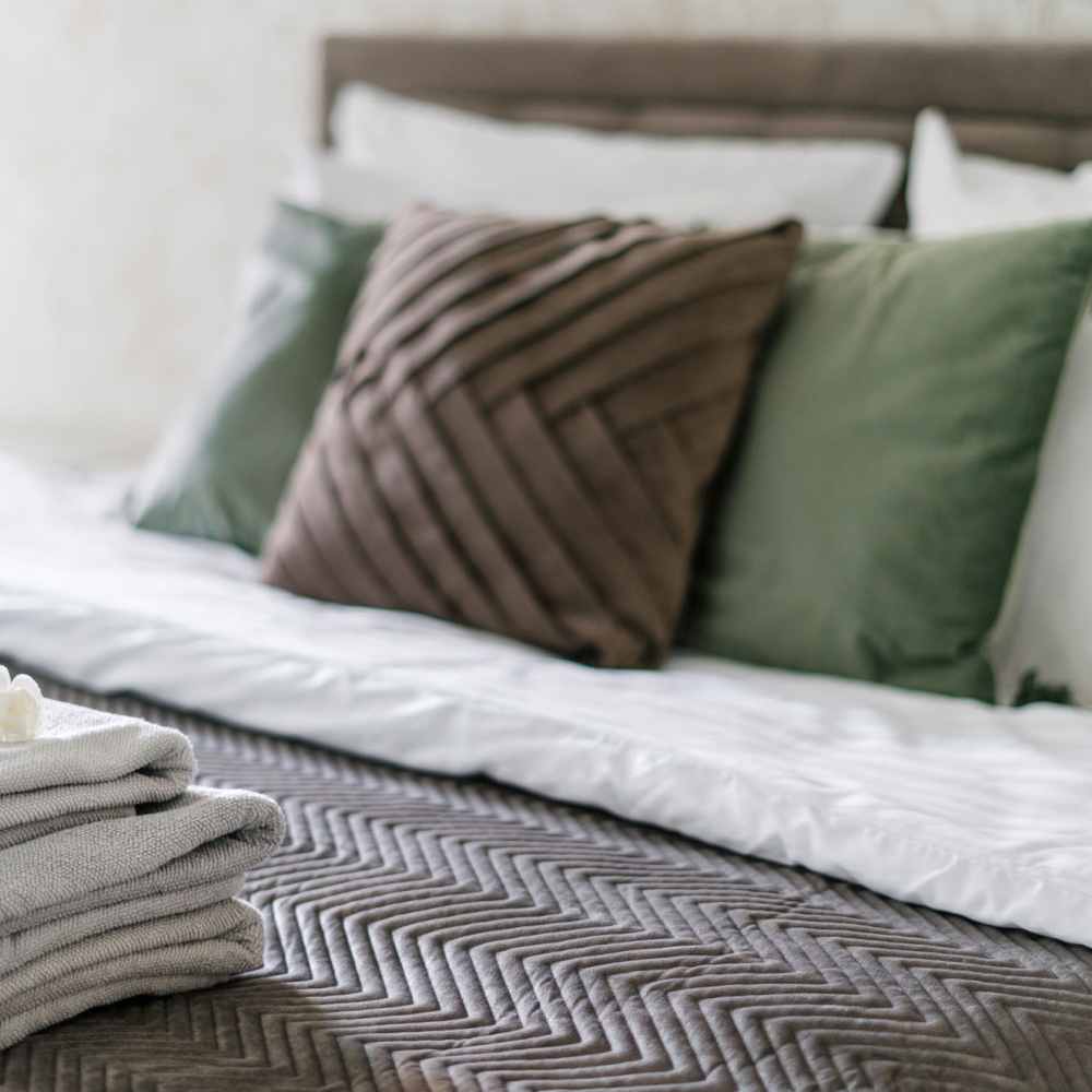 Bedroom with stacked gray towels on a patterned bedspread at Atrium Gardens in Arlington, Texas