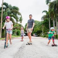 Family skateboarding and scootering on palm-lined street at The Nathaniel in Rochester, New York