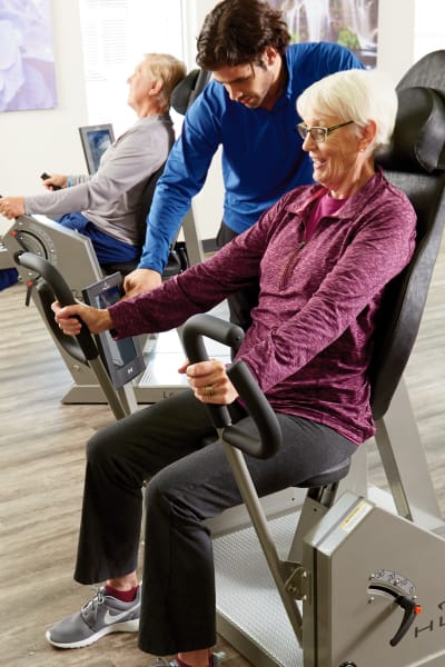 Gym instructor assisting a resident on a workout machine at Quail Park of Lynnwood in Lynnwood, Washington