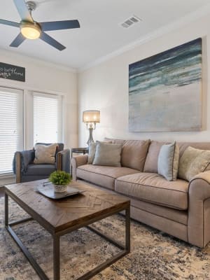 Model living room with a ceiling fan and private balcony access at Auberge of Burleson in Burleson, Texas