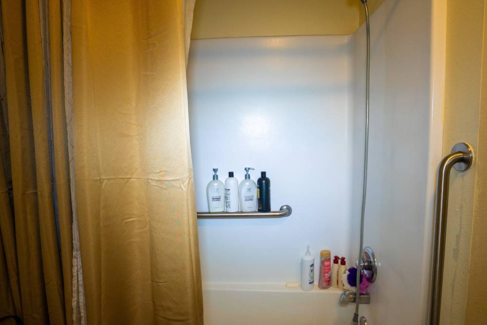 Shower with beige curtain and various bottles on a shelf at Willowbrook I in Lafayette, Louisiana