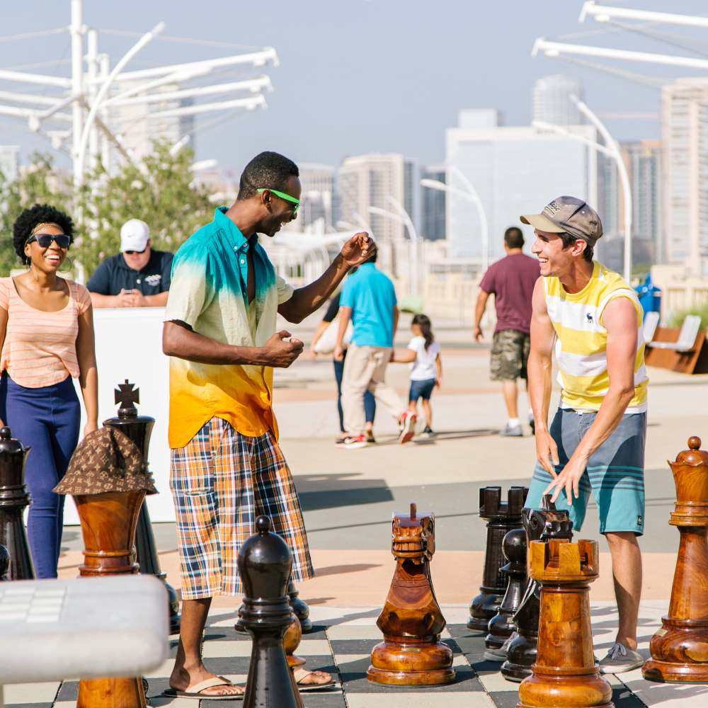 Residents playing with oversized chess pieces in outdoor setting near Pike West Commerce in Dallas, Texas