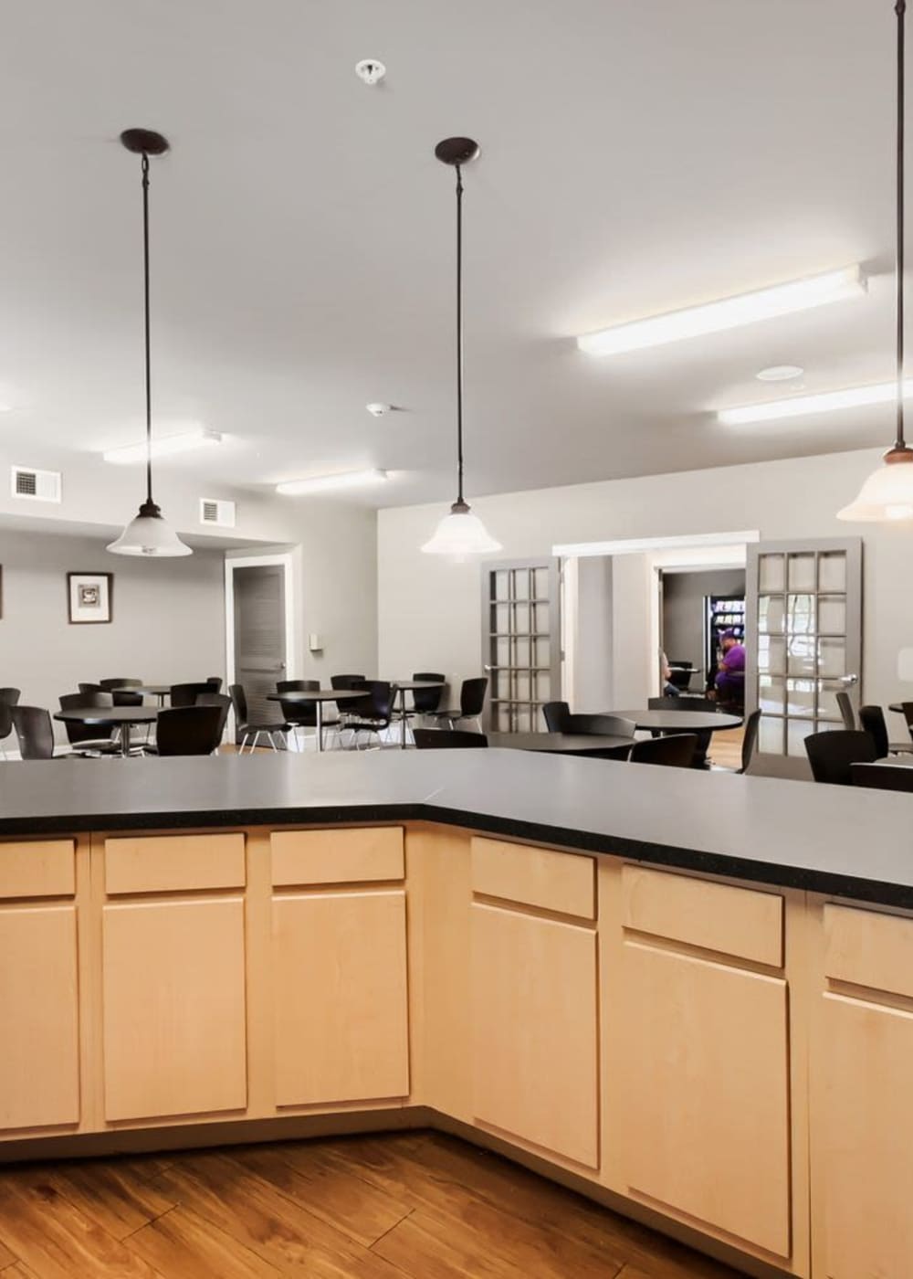 Modern community kitchen with wood-style flooring, pendant lights, and ample seating for residents at Lindbergh Parc Senior Apartments in Fort Worth, Texas