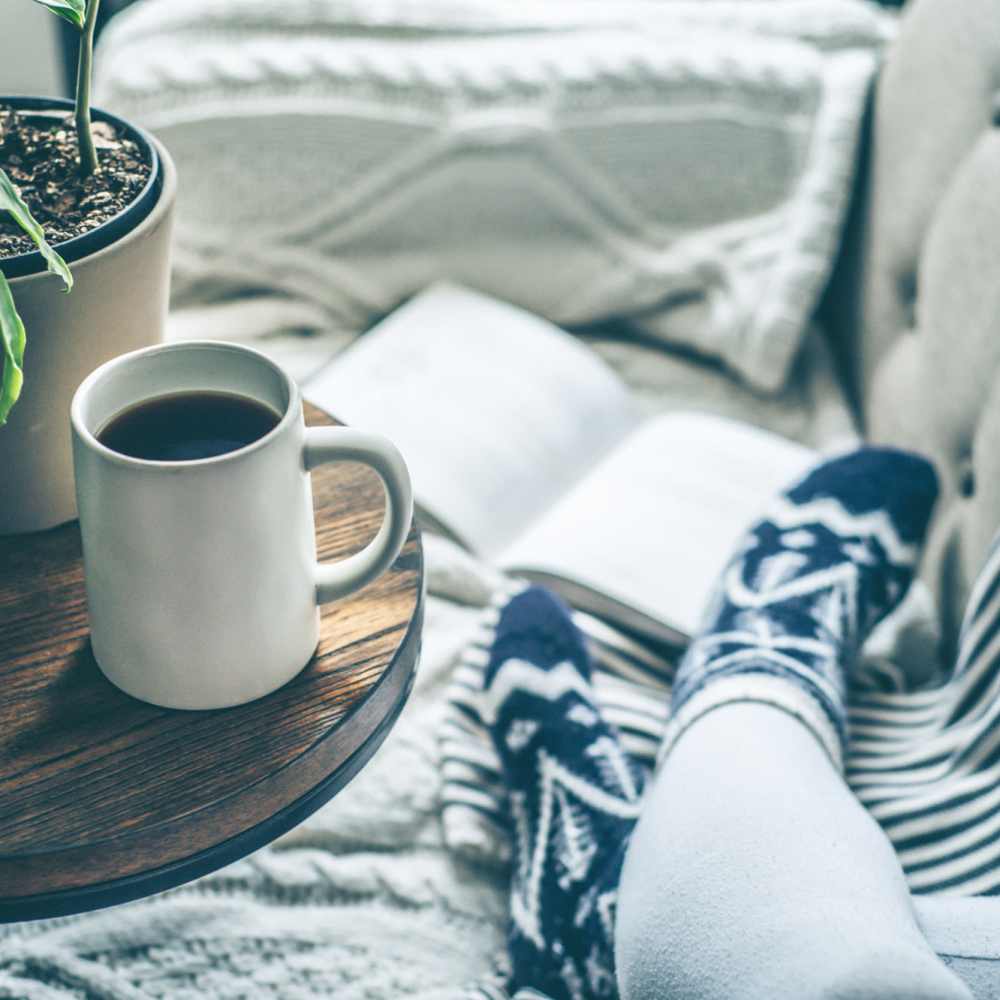 Resident relaxing in their living room with a cup of coffee and a book at The Elms at Kendall Ridge in Columbia, Maryland
