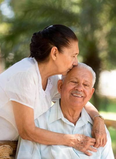 Daughter kissing her father on the head outside on a beautiful day at Arcadia Senior Living Pace in Pace, Florida