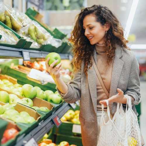 Woman selecting fresh green apples in vibrant grocery aisle at Standard at Royal Lane in Dallas, Texas