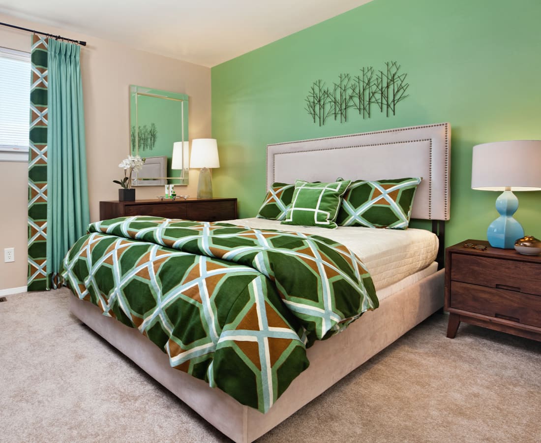 Model bedroom with plush carpeting and a green accent wall at James River Pointe in Richmond, Virginia