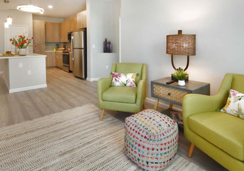 Bright living room with green chairs and modern kitchen view at Messina Luxury Apartments in New Smyrna Beach, Florida