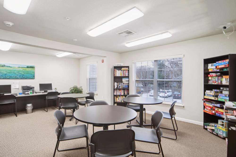 Bright community room with tables, computers, and bookshelf setup at Villas At Meadow Springs in Ankeny, Iowa