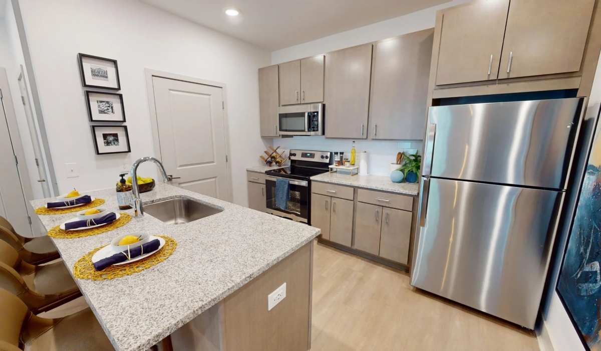 Modern kitchen in The Altitude floor plan at Elevation 800, featuring stainless steel appliances, granite countertops, light wood cabinetry, and a large island with bar seating.