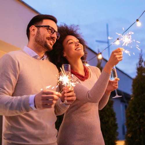 Resident couple with sparklers at twilight on the private balcony outside their home at Reserve at Peachtree Corners in Norcross, Georgia