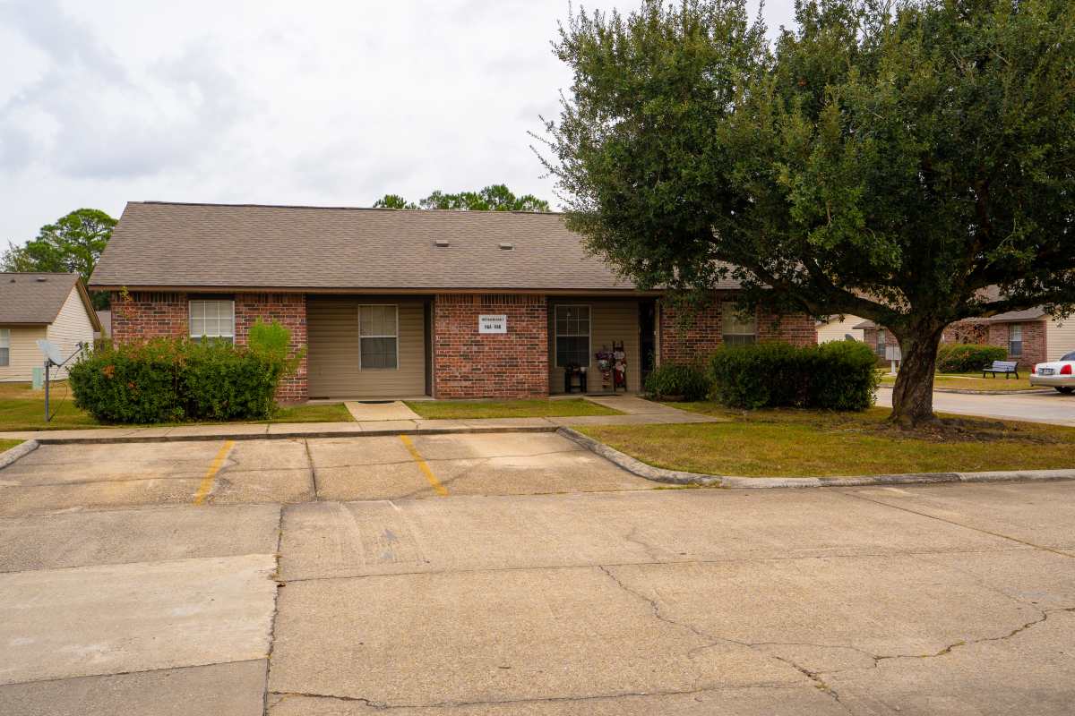 Single-story brick apartment with landscaped front yard and parking spaces visible at Willowbrook I in Lafayette, Louisiana