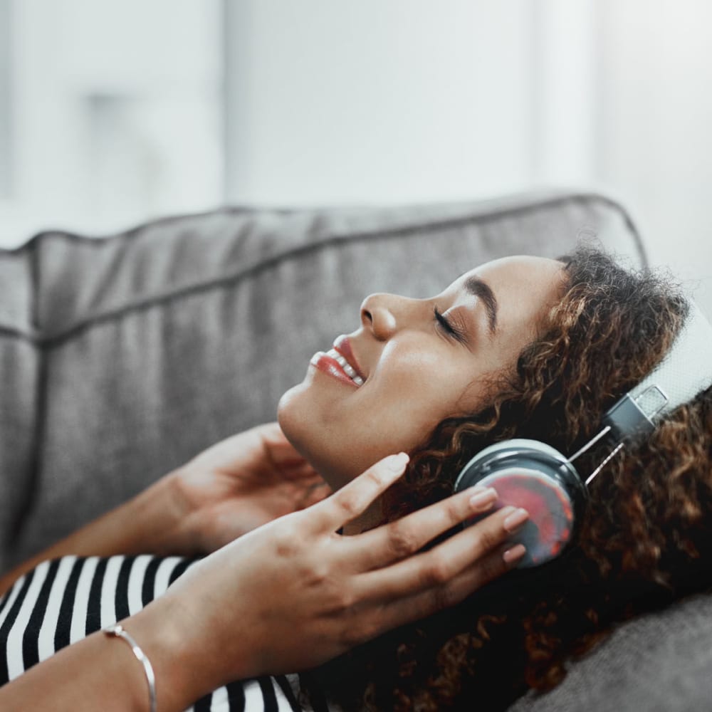 Resident jamming to some tunes on headphones from the comfort of her couch at Oaks Riverchase in Coppell, Texas