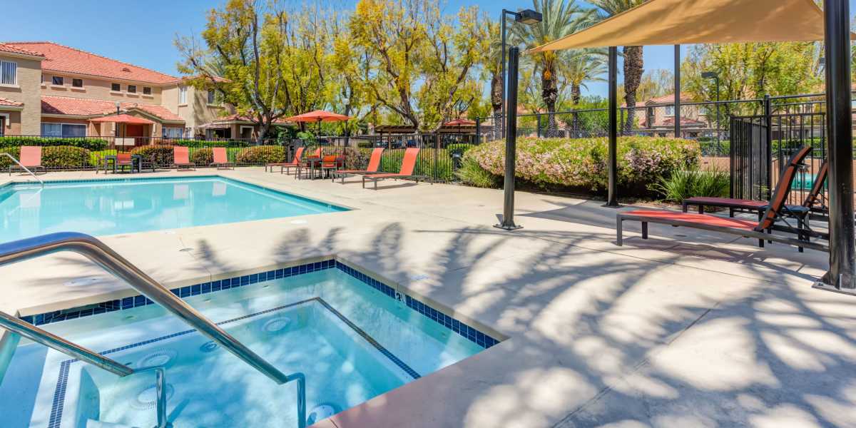 Spa and pool with lounge chairs and umbrellas at Tuscany Village Apartments in Ontario, California