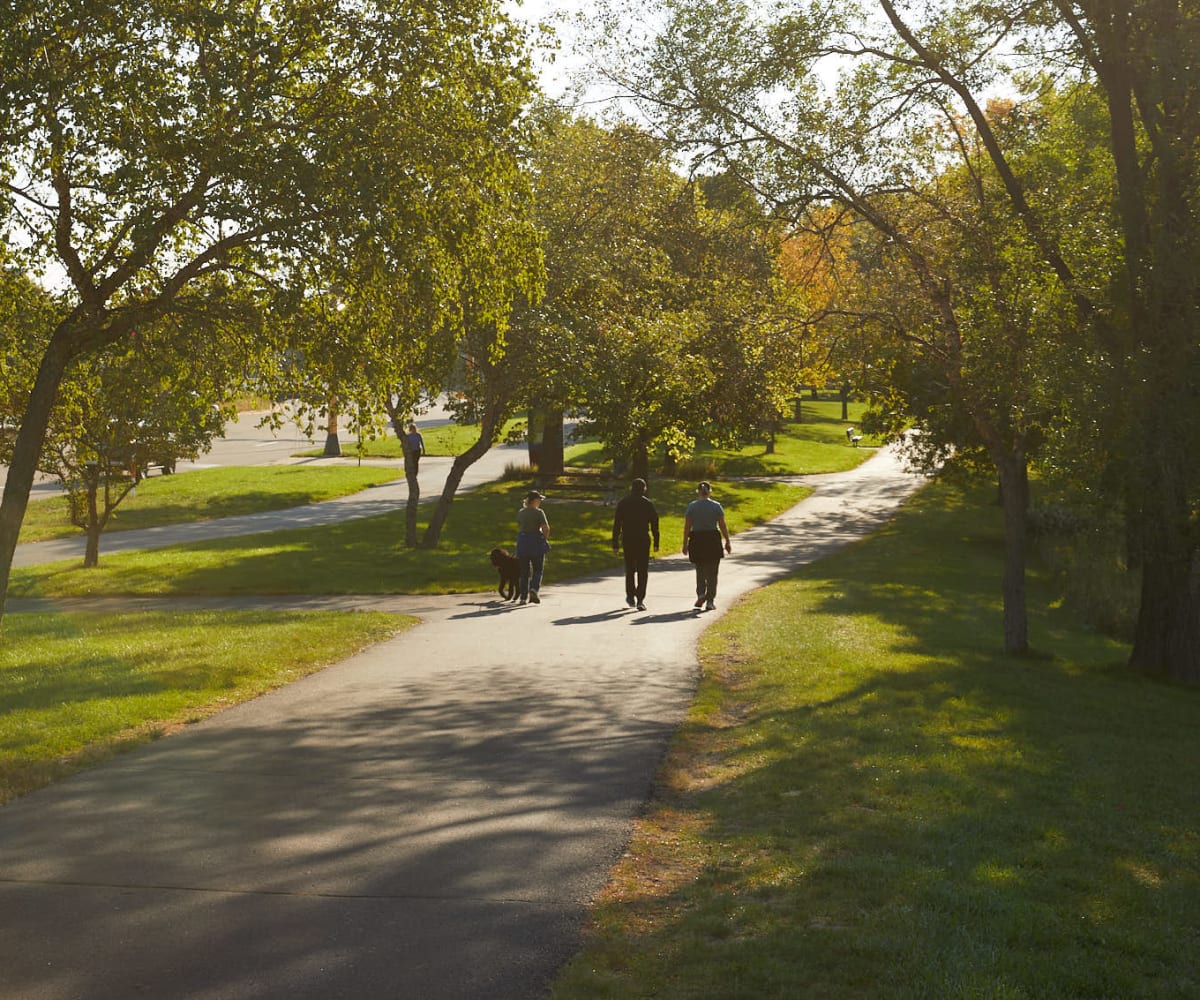 Three residents walking outdoors on a paved walking path surrounded by beautiful greenery at Amira in Bloomington, Minnesota