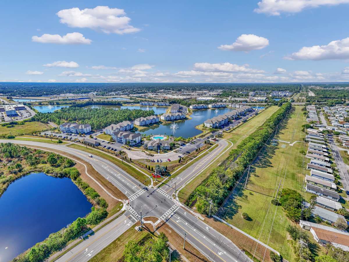 Aerial view of a resort-style apartment community with sparkling pool and nearby lakes at The Carlton of West Melbourne in West Melbourne, Florida