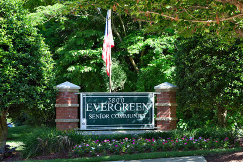 Sign for Evergreen Senior Community surrounded by lush greenery and colorful flower beds at Evergreen Senior Community in Bowie, Maryland