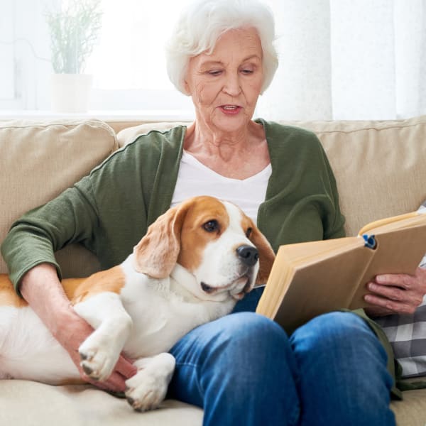 Resident reading a book while holding her pet dog at Courtyard at Coeur d'Alene in Coeur d'Alene, Idaho