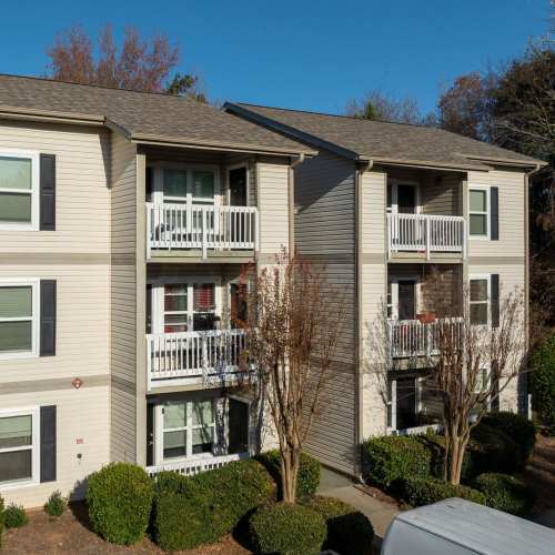 Three-story apartment building with balconies, landscaped bushes, and trees lining the exterior at Pleasant View Apartments in Charlotte, North Carolina