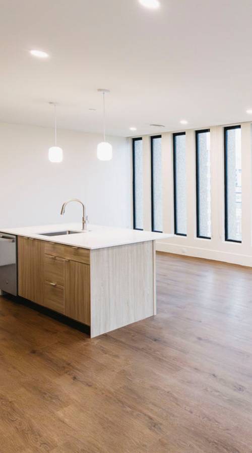 Open‑concept living space with wood floors, kitchen island, and tall floor‑to‑ceiling windows at Residences at 111 Lyon in Grand Rapids, Michigan