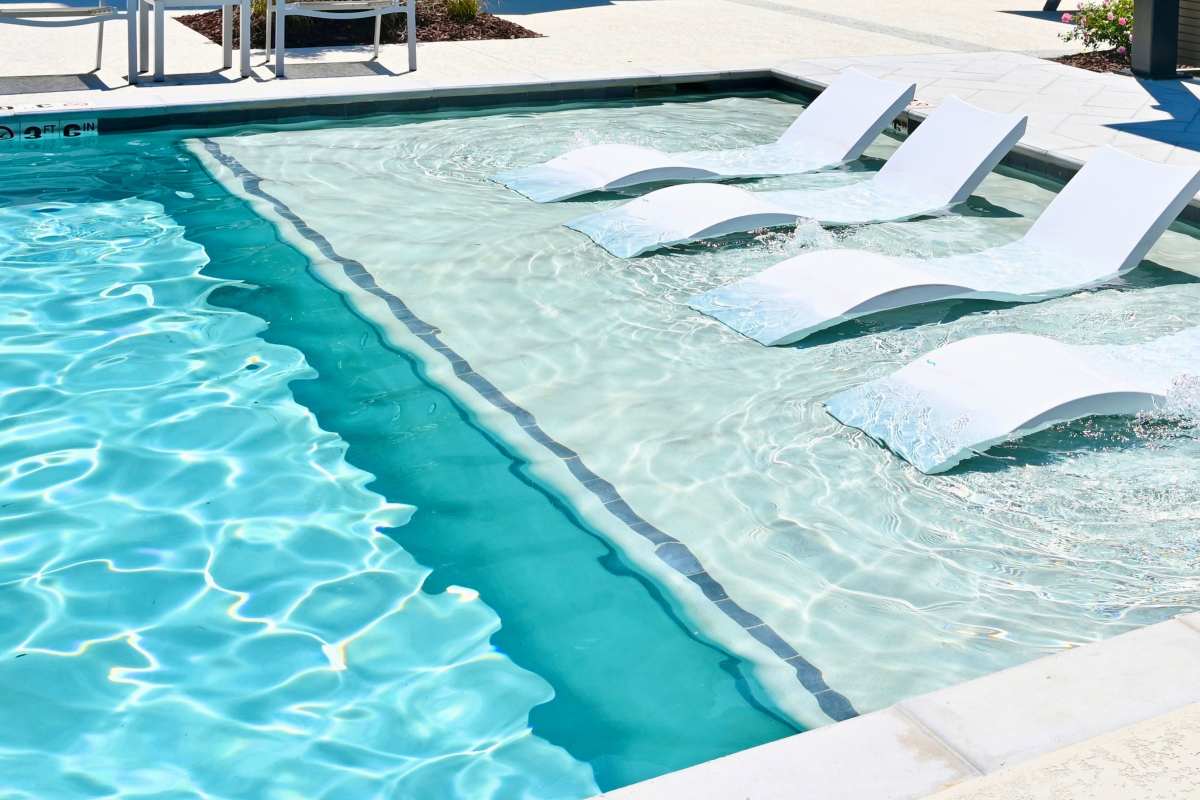 crystal clear swimming pool waters reflects a teal tint next to reclined white pool shelf chairs offering a relaxing way to enjoy the baja pool shelf while tanning or socializing by the resort style pool and outdoor lounge