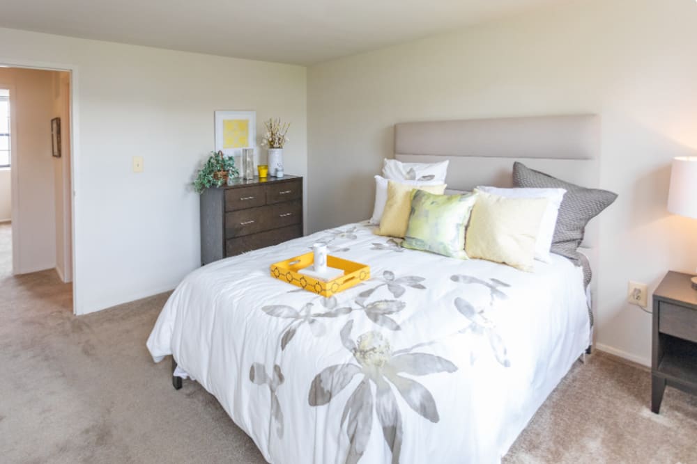 Cozy bedroom featuring a comfortable bed, decorative pillows, and a stylish dresser with plants at Dutch Village Apartments in Baltimore, Maryland