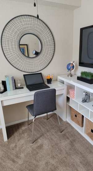 A home office with a white des, chair and white shelves and large round mirror hangs on the wall at The Abbey At Northlake in Riviera Beach, Florida
