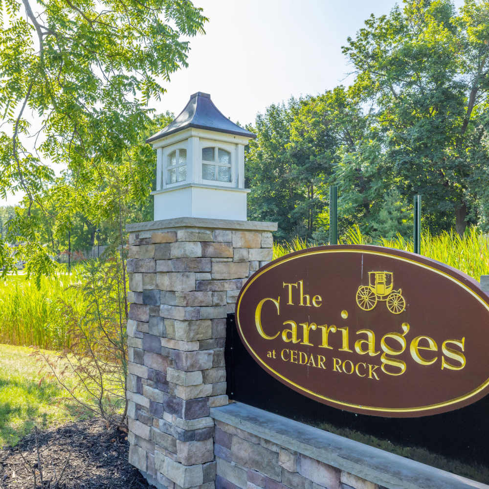 Gated entrance sign with stone pillars and greenery in the background at Carriages At Cedar Rock in Webster, New York