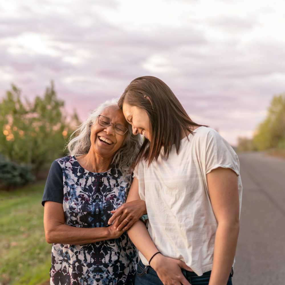 Two women laughing together outdoors, enjoying a joyful moment in a lush green setting at Lindbergh Parc Senior Apartments in Fort Worth, Texas