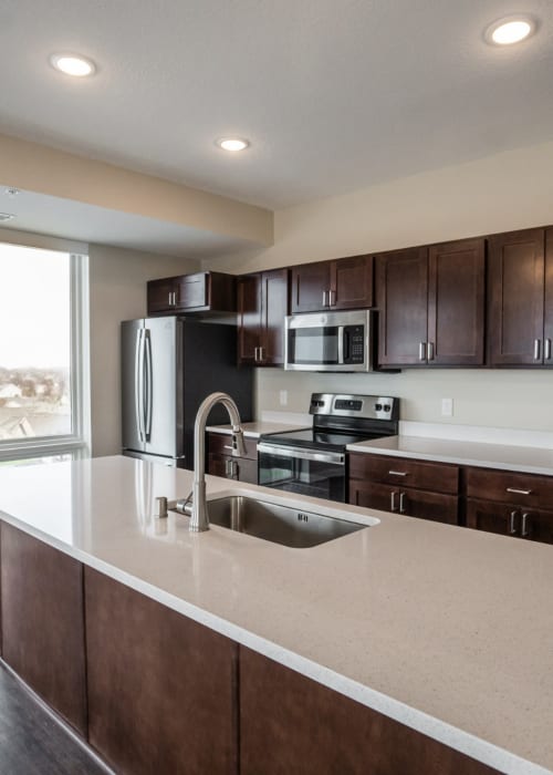 Apartment kitchen with granite countertops and dark wooden cabinets at The Pillars of Hermantown in Hermantown, Minnesota