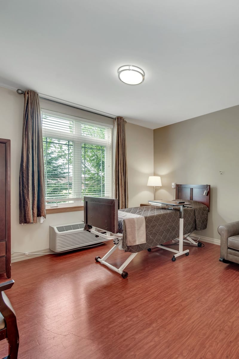 Transitional care room with a bed next to a large window and hardwood floors at Fair Oaks Health Care Center in Crystal Lake, Illinois