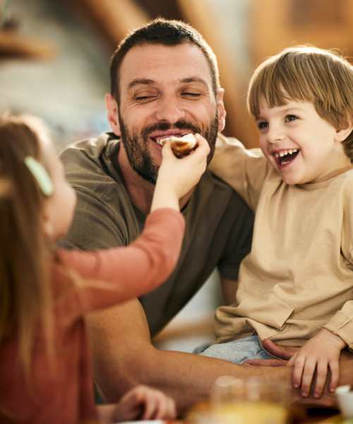 Father enjoying snack time with two smiling children in a cozy kitchen at Monarch Station in Louisville, Kentucky