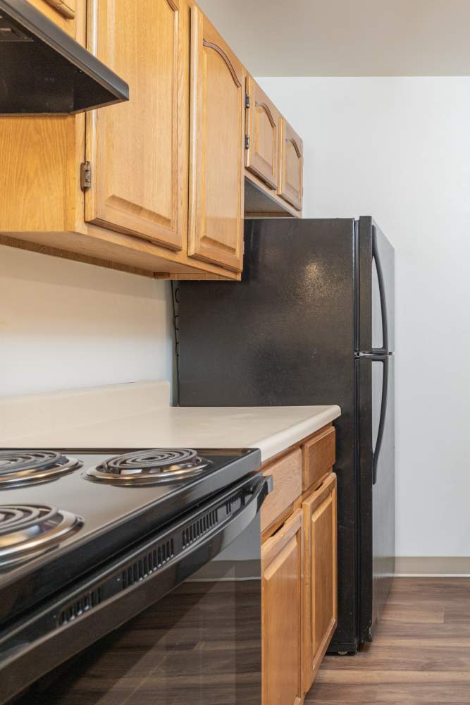 Kitchen with wood-tone cabinets and black appliances at Squires Manor Apartment Homes in South Park, Pennsylvania