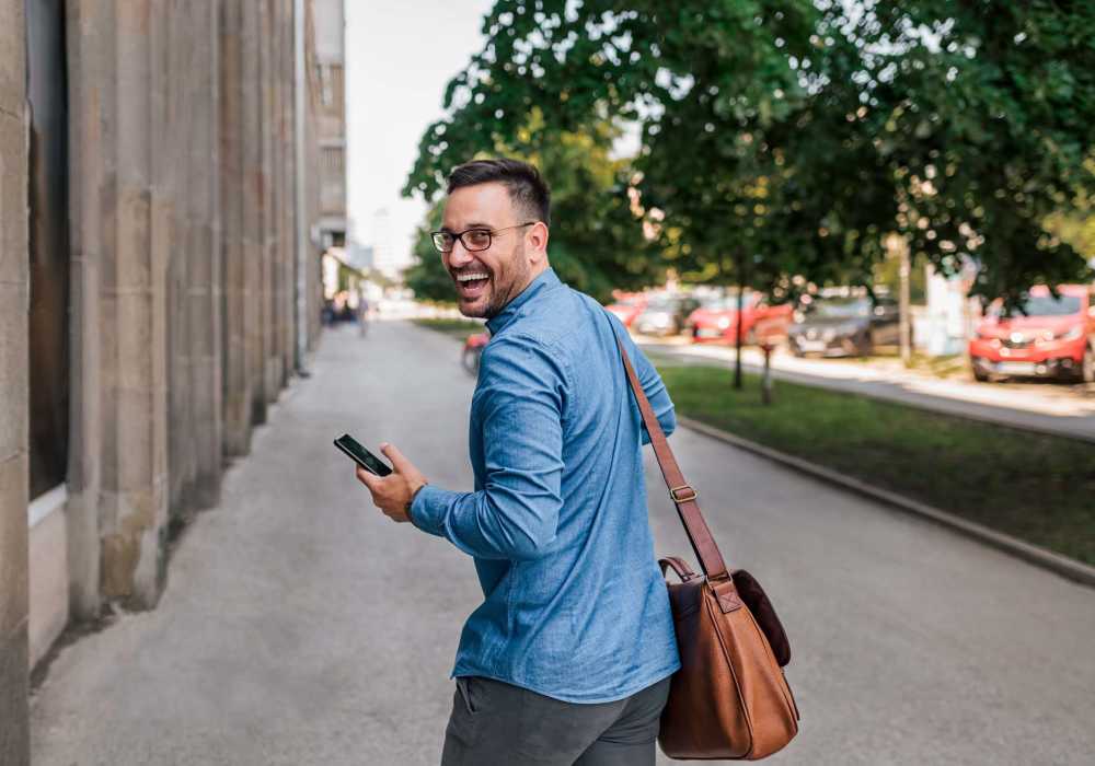 Casual man walking with smartphone and leather bag in city street at Messina Luxury Apartments in New Smyrna Beach, Florida