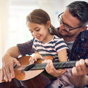 Father playing guitar with his daughter in their new home at Vista Park in Dallas, Texas