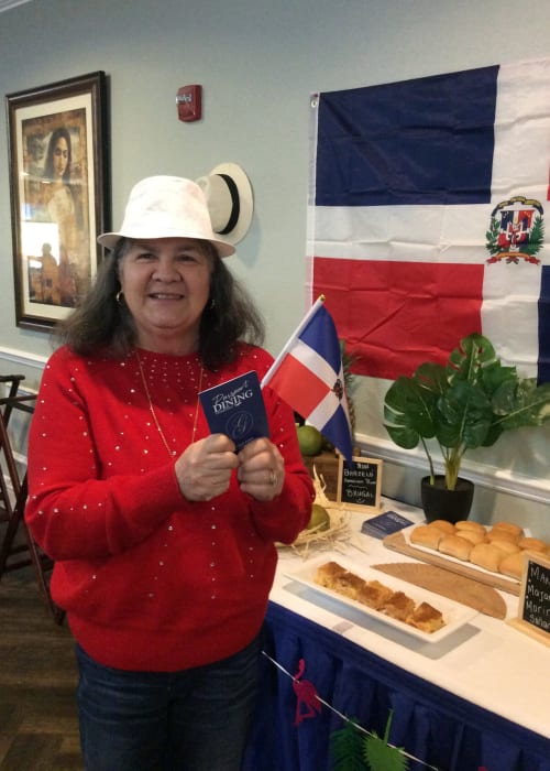 Resident posing for a photo in front of international dishes at a passport dining event at Grand Villa of Palm Coast in Palm Coast, Florida